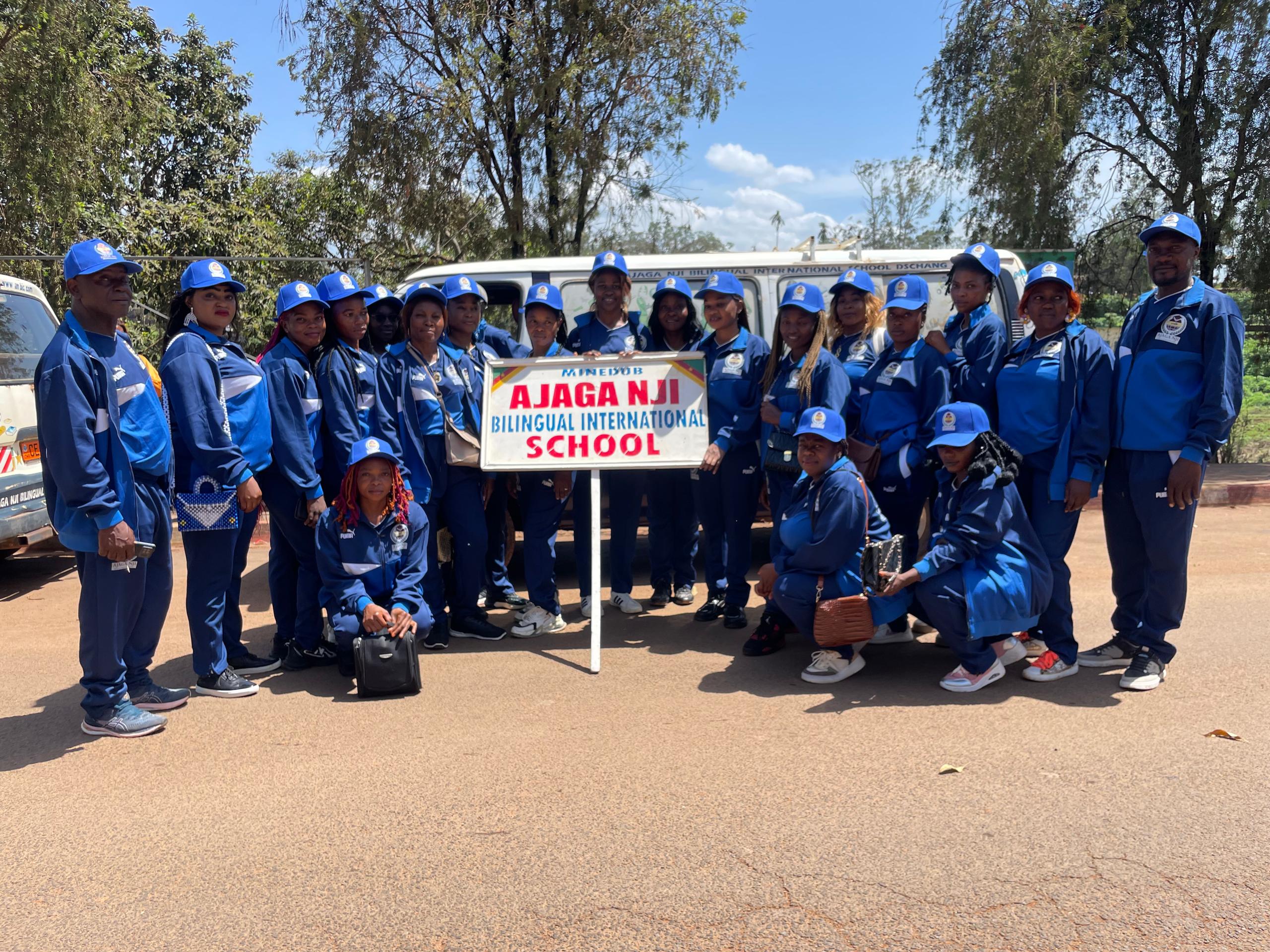 Ajaga Nji school group in blue tracksuits holding the school sign beside a bus